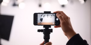 Person records video, phone, tripod, lights.